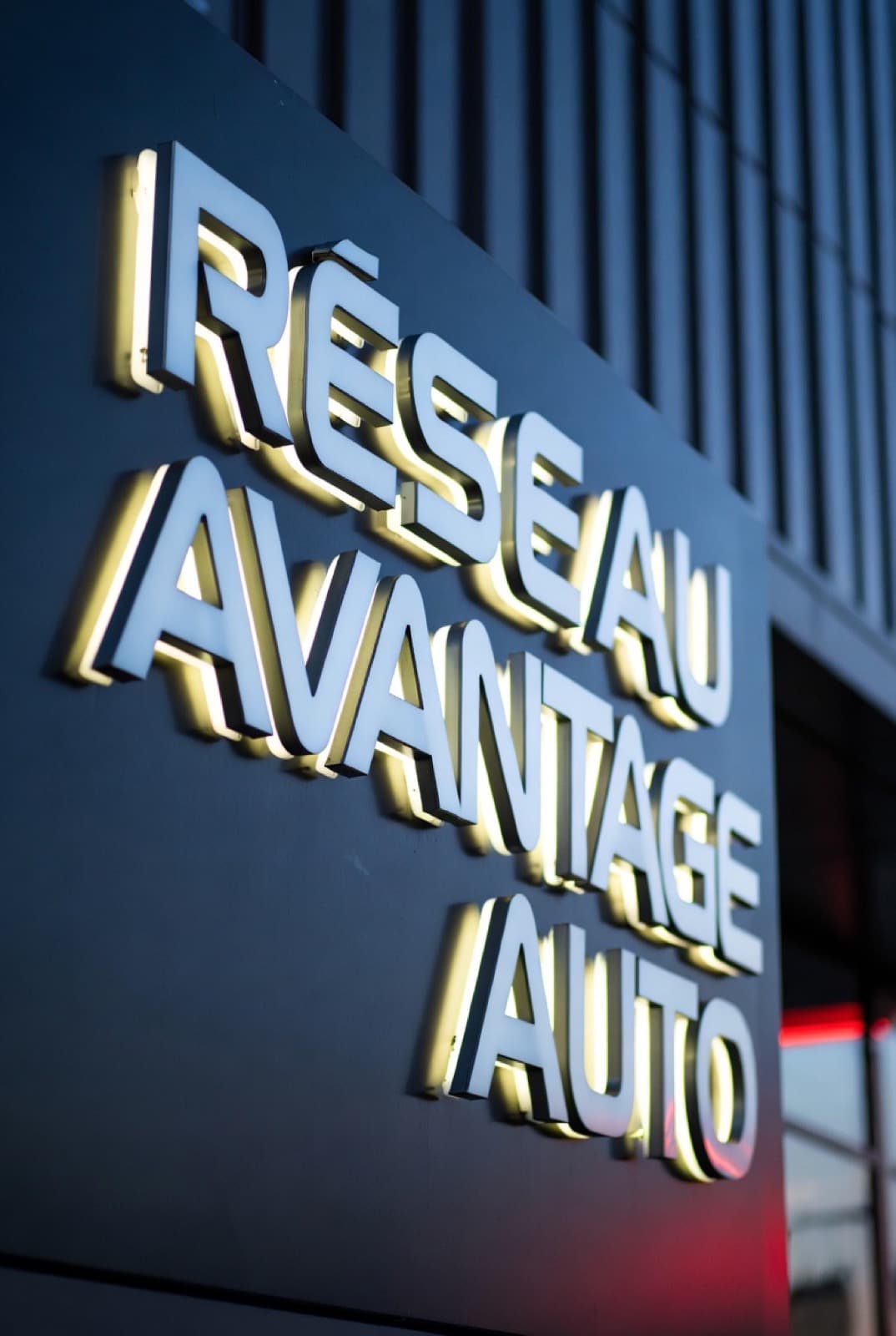 L'enseigne lumineuse Réseau Avantage Auto sur la façade de l'agence, à la nuit tombée